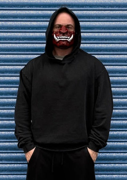 man in black acid wash hoodie in front of steel shutters with oni mask