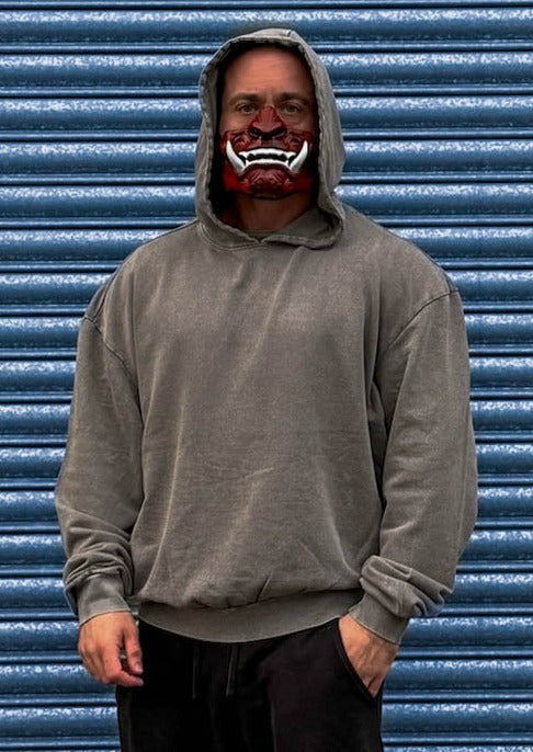 man in grey acid wash hoodie in front of steel shutters with oni mask