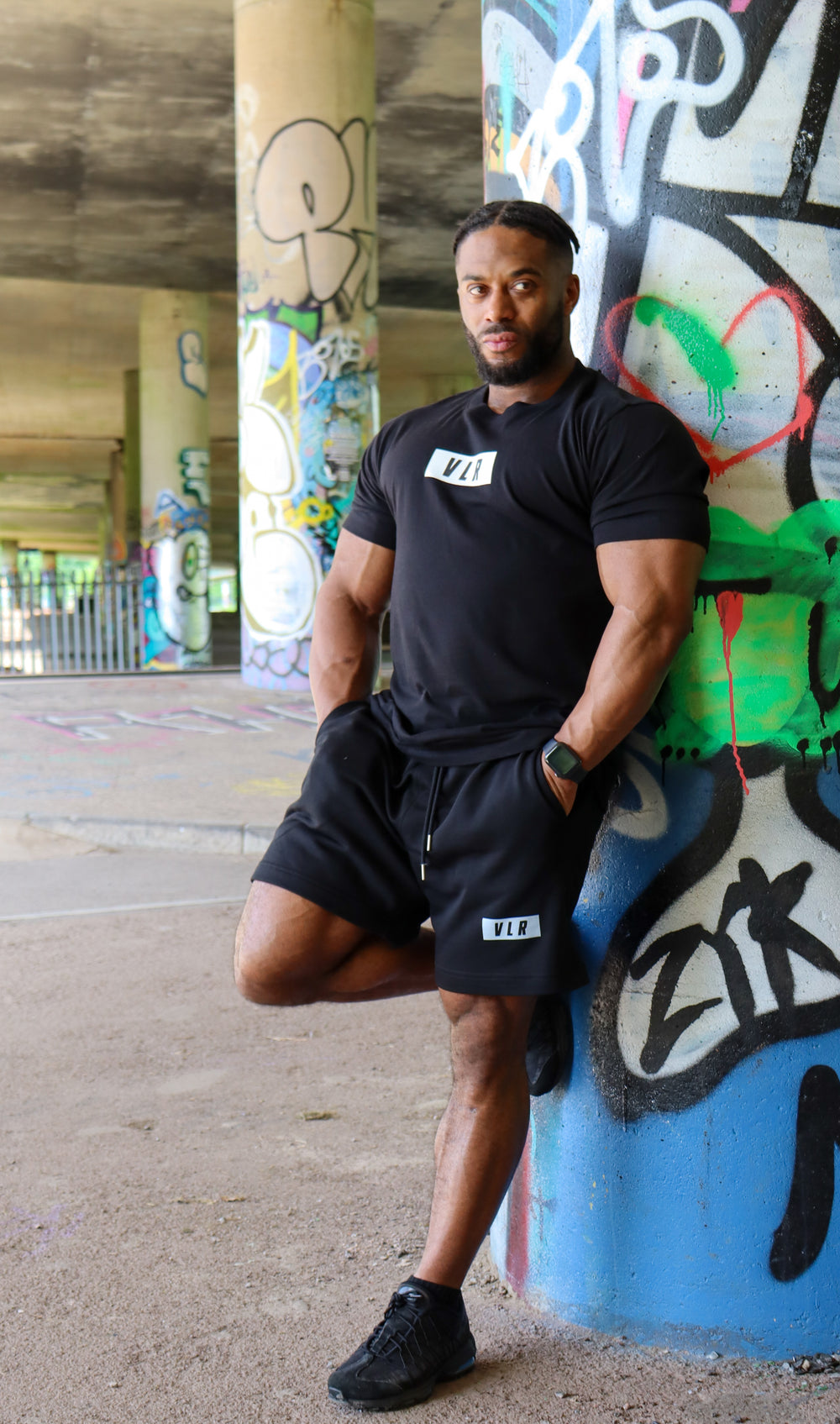 bodybuilder in black valour shirt under bridge graffiti